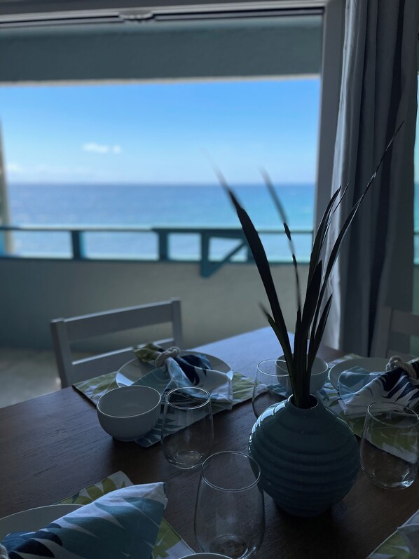 A dining table with a view of the ocean, a vase with green leaves, and empty glasses. - Ocean front Tortuga Bliss condo - close beach (St Thomas)