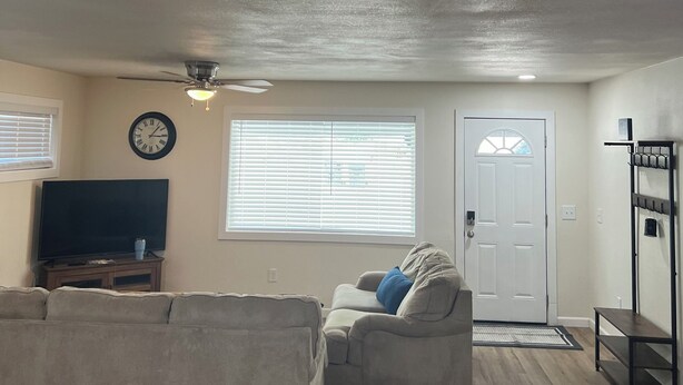 Ein Wohnzimmer mit einer Couch, einem Fernseher, einem Deckenventilator und einer Tür.