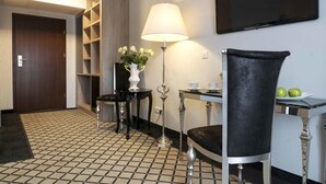 A hotel room with a checkered floor, a desk with a lamp, a chair, a TV mounted on the wall, and a door leading to another room. - Pałac na Wodzie  (Podgorzyn)