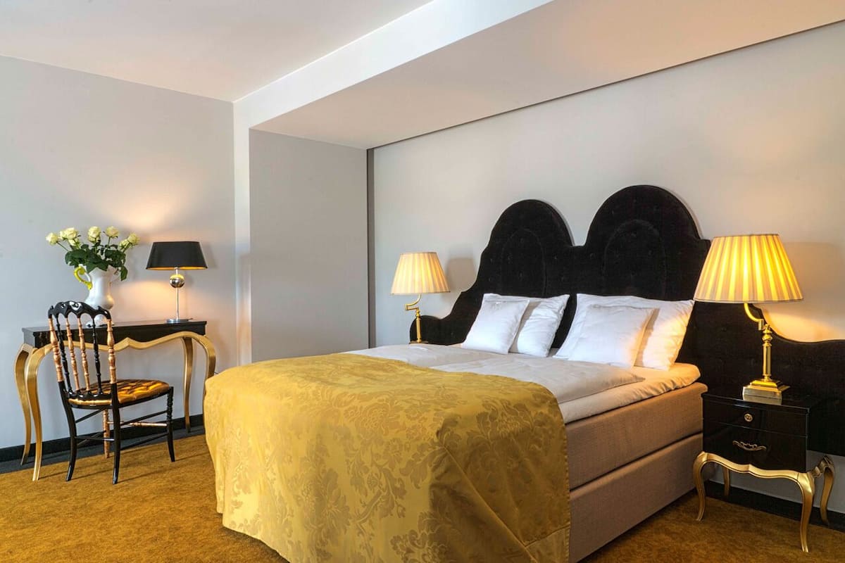 A hotel room with a large bed, two bedside tables with lamps, a chair, and a small table with a vase of flowers.