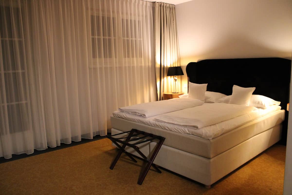 A neatly made bed with white linens, a black headboard, and a bedside lamp.