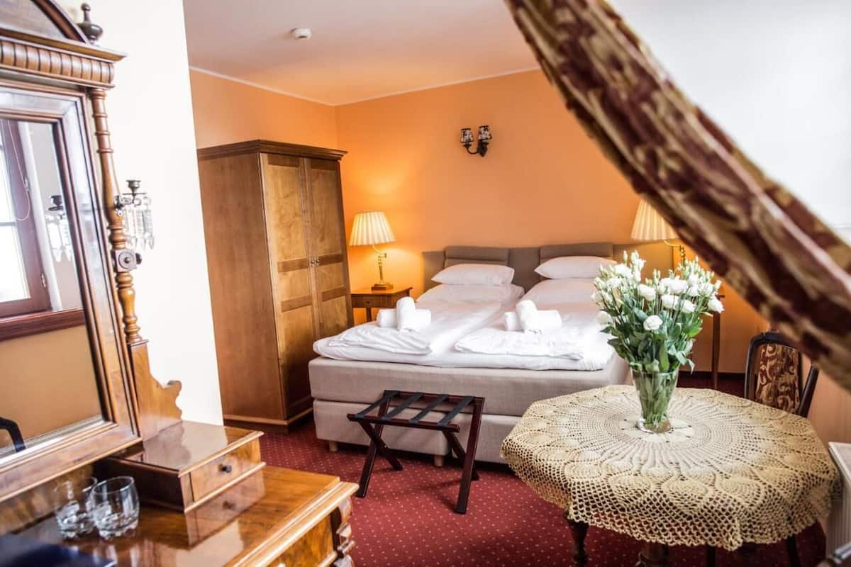 A hotel room with a bed, a wooden wardrobe, a small table with a lace tablecloth, and a vase with flowers.