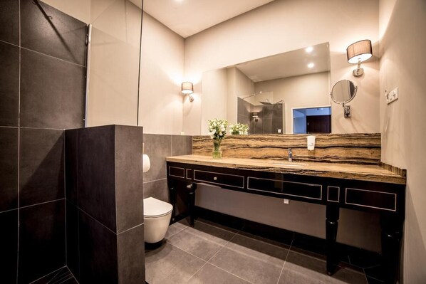 A modern bathroom with dark tiles, a marble countertop, a large mirror, and a shower area.