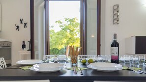 Ein Esszimmertisch ist gedeckt mit Tellern, Gläsern, Besteck und einer Weinflasche, mit Blick auf grüne Pflanzen.