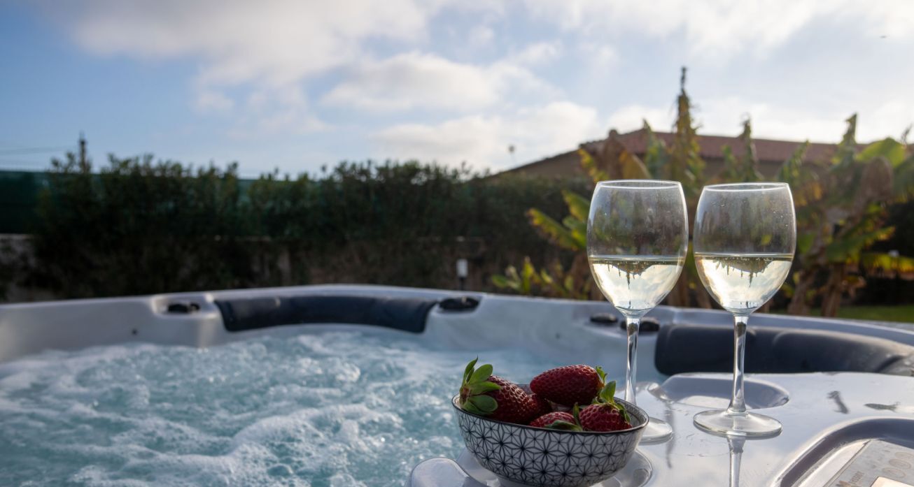 A hot tub with two glasses of white wine and a bowl of strawberries.