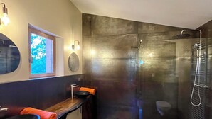 A modern bathroom with a glass-enclosed shower, a wooden bench, a round mirror, and a black sink. - le Charme D'une Cabane, le Confort en Plus (Aups)