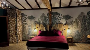 A bedroom with a bed, a wooden headboard, a wall mural of trees, and a stack of logs. - le Charme D'une Cabane, le Confort en Plus (Aups)