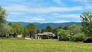 A rural landscape with a field of yellow flowers, a rustic house, and a backdrop of green hills. - le Charme D'une Cabane, le Confort en Plus (Aups)