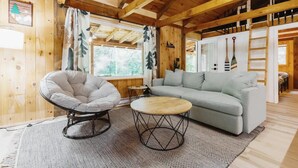 A cozy cabin interior with a round wooden table, a grey sofa, and a bean bag chair.