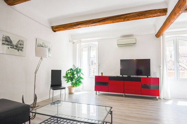 Un salon moderne avec une table basse en verre, un meuble de rangement rouge et noir pour les appareils électroniques, une plante en pot et un fauteuil noir.