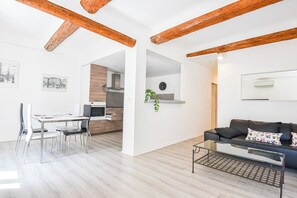 Un salon moderne comprenant un coin repas, une cuisine et des poutres en bois au plafond.