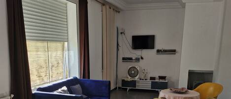 A living room with a blue sofa, a yellow sofa, a flat-screen TV mounted on the wall, and a fireplace.