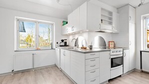 A modern kitchen with white cabinetry, a built-in oven, and a window with a view of trees. - 2 bedroom amazing home in Sørvad (Sørvad)