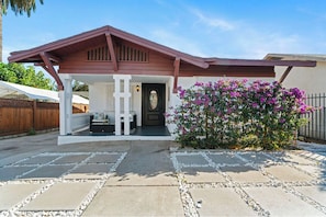 Enjoy a peaceful retreat with a covered porch, bench, and table, surrounded by lush greenery and a beautifully paved entrance.