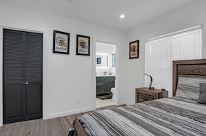 Cozy retreat with a large bed, nightstand, and framed picture, leading to a bathroom with a sink and mirror.