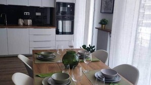 Eine moderne Küche mit weißen Schränken, einem eingebauten Backofen und einem Essbereich mit einem Holztisch für vier Personen.