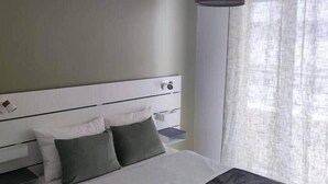 Ein Schlafzimmer mit Bett, Nachttisch, Lampe und einem Fenster mit Vorhängen.