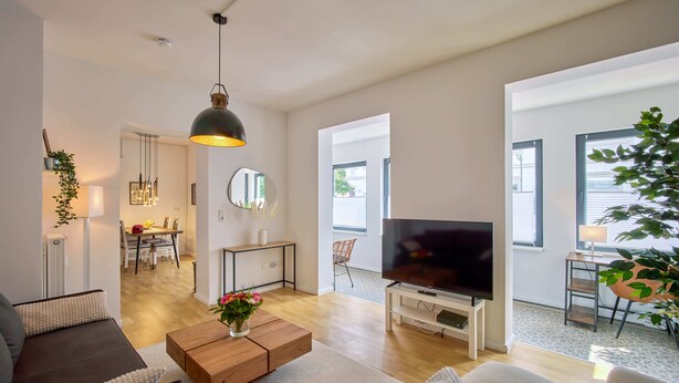 Een moderne woonkamer met een flatscreen televisie, een houten salontafel en een eethoek met een stoel en tafel.