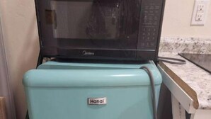 Ein türkis-farbener Kühlschrank mit einer Mikrowelle darauf, einem Schild mit der Aufschrift 'Hana' und einer weißen Arbeitsplatte im Hintergrund.