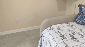 Ein Schlafzimmer mit einem Bett, einem an der Wand montierten Fernseher und einem kleinen Regal darunter.