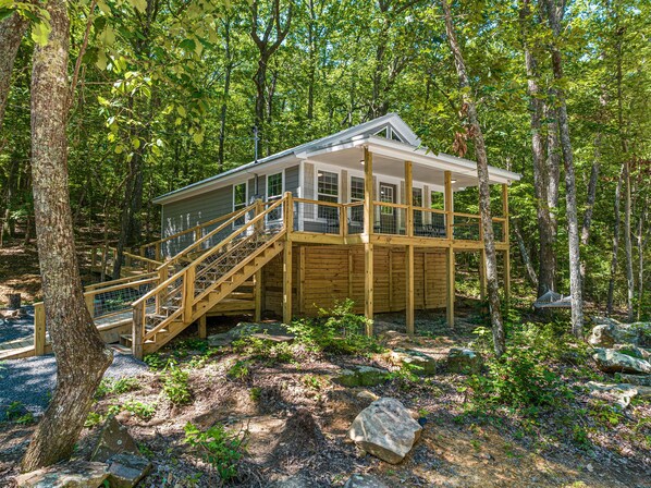 Una cabaña de madera con terraza y escaleras, rodeada de árboles.