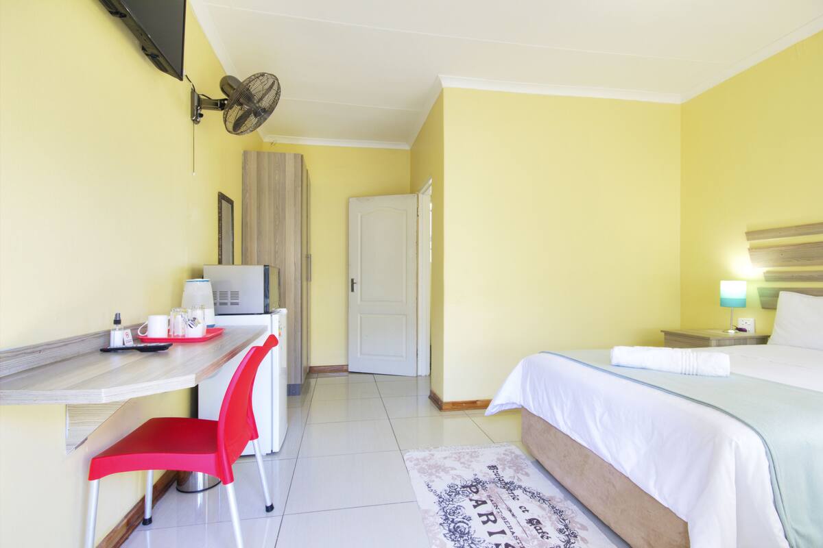 A hotel room with a bed, a desk with a chair, a television, and a fan.