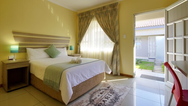 A hotel room with a bed, bedside table, lamp, and a view of the outside. - Minilitha Lodge (Richards Bay)