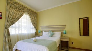 A hotel room with a large bed, a nightstand, a bedside table, a mirror, and curtains. - Minilitha Lodge (Richards Bay)