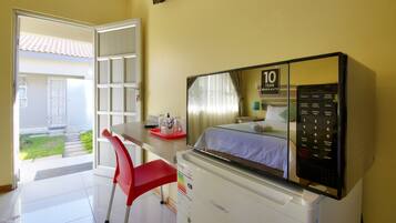 A hotel room with a bed, a desk with a red chair, a TV, and a control panel.