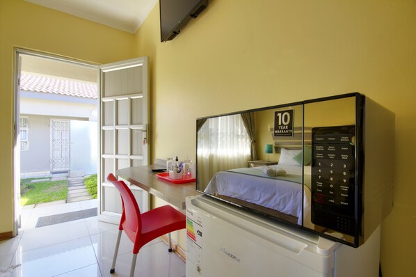 A hotel room with a bed, a desk with a red chair, a TV, and a control panel. - Minilitha Lodge (Richards Bay)