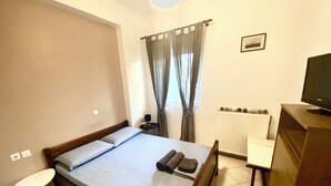A bedroom with a bed, a desk, a chair, a television, and a window with curtains.