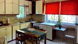A kitchen with wooden cabinets, a dining table with chairs, a window with red blinds, and a hanging light fixture.