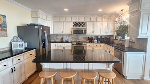 A modern kitchen with white cabinets, a black countertop, and a central island with stools. - Cozy, Colorful, Coastal Cottage - Oceanfront 5 bedroom home (Ocean Isle Beach)