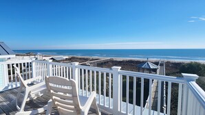 A wooden deck with white railings overlooking a beach. - Cozy, Colorful, Coastal Cottage - Oceanfront 5 bedroom home (Ocean Isle Beach)
