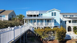 A coastal house with a covered porch, a second-story balcony, and a wooden deck. - Cozy, Colorful, Coastal Cottage - Oceanfront 5 bedroom home (Ocean Isle Beach)