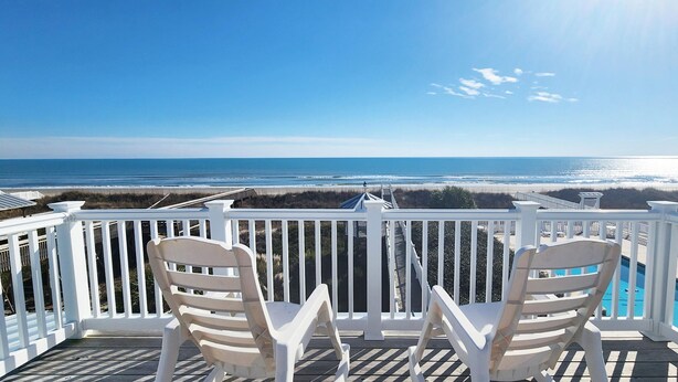 A balcony with white railings, two white chairs, and a view of the ocean. - Cozy, Colorful, Coastal Cottage - Oceanfront 5 bedroom home (Ocean Isle Beach)