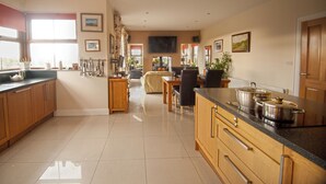 A spacious kitchen with wooden cabinets, a dining area with a table and chairs, and a living room with a sofa. - Luxury 4-bed House in Craigavon (Craigavon)
