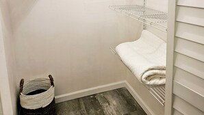 Ein Schrank mit Kleiderhänger, einem gefalteten Handtuch und einem Korb.