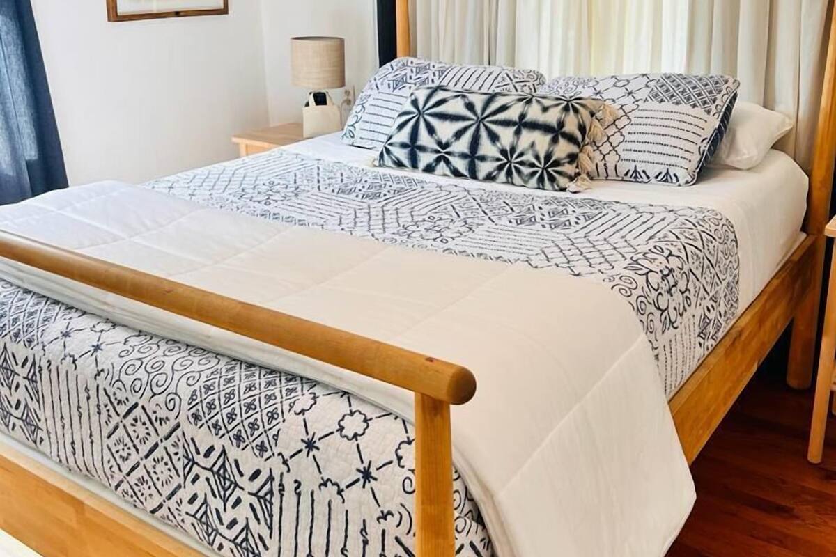 Una cama con colcha y almohadas estampadas, un cabecero de madera y una mesita de noche con una lámpara.