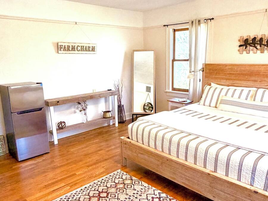 A bedroom with a bed, a refrigerator, a bedside table, a mirror, and a wall-mounted artwork.