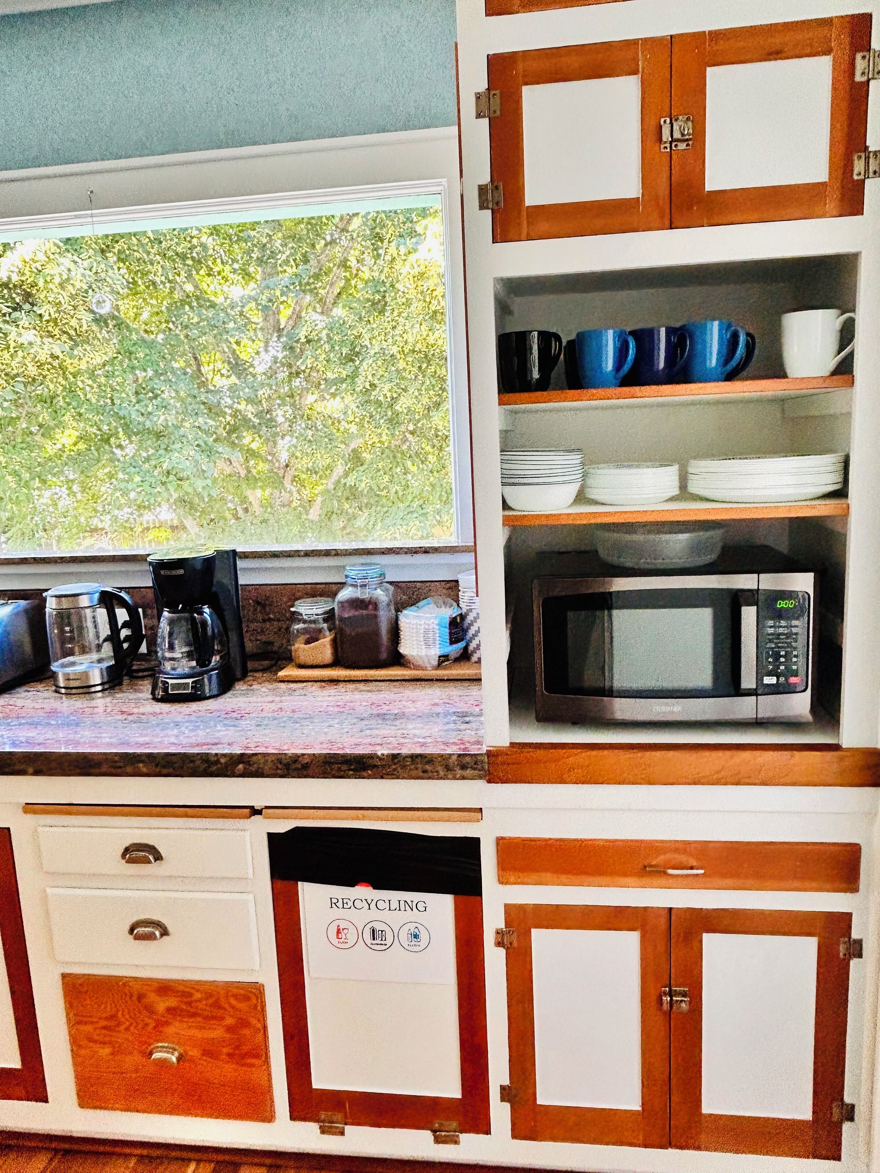Une cuisine avec une fenêtre, un four à micro-ondes et une poubelle de recyclage.
