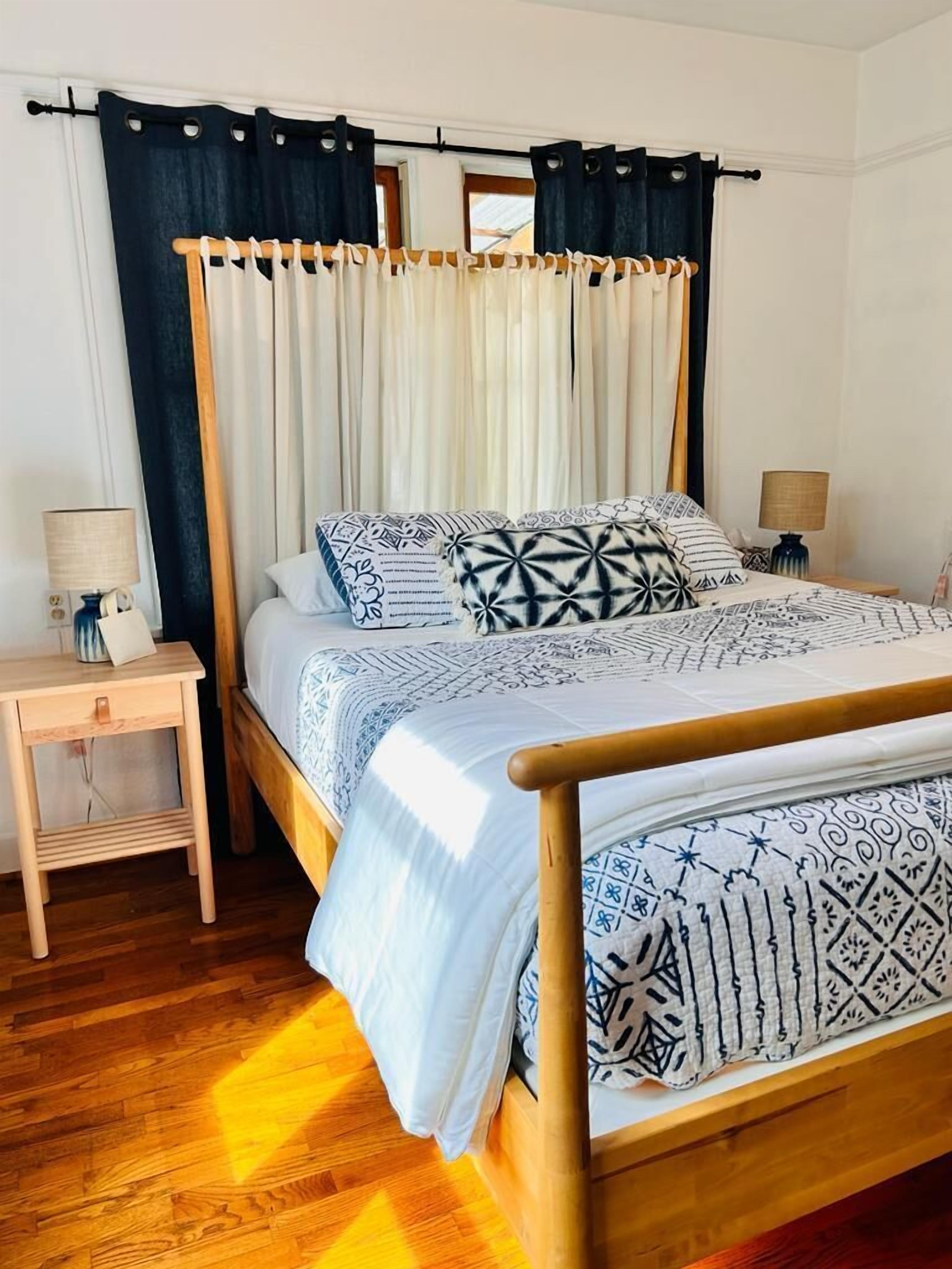 Una cama bien tendida con ropa de cama estampada, un cabecero de madera y una mesita de noche con una lámpara.