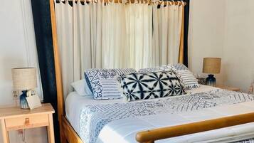 Una cama bien tendida con ropa de cama estampada, un cabecero de madera y una mesita de noche con una lámpara.