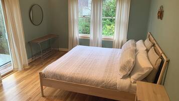 A bedroom with a wooden bed, white bedding, a wooden nightstand, a bench, and a window with curtains.