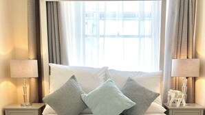 Uma cama de dossel com colcha acolchoada, duas luminárias de cabeceira e uma mesa de cabeceira com objeto decorativo.
