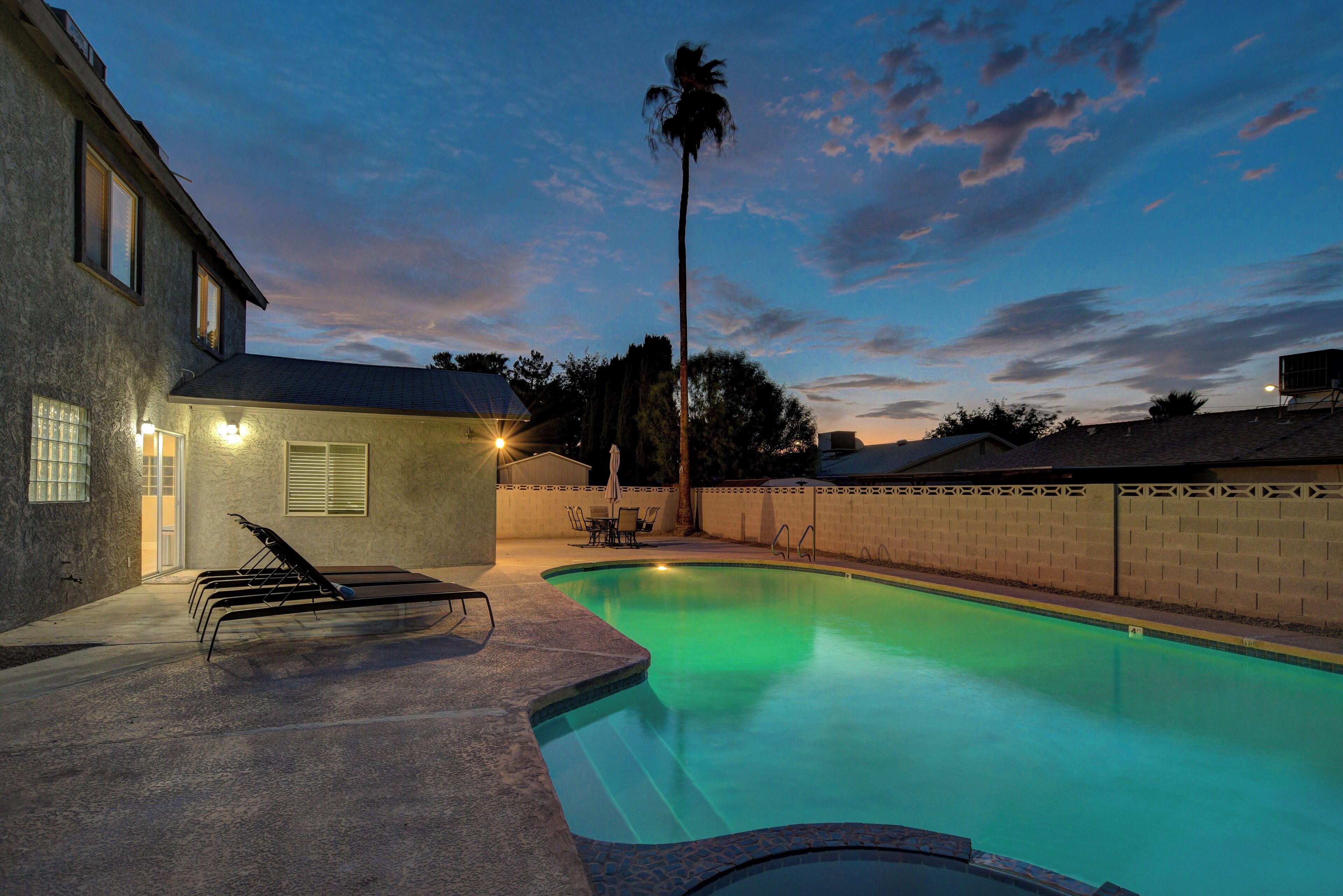 A swimming pool with a sunlit patio area, a tall palm tree, and a brick wall.