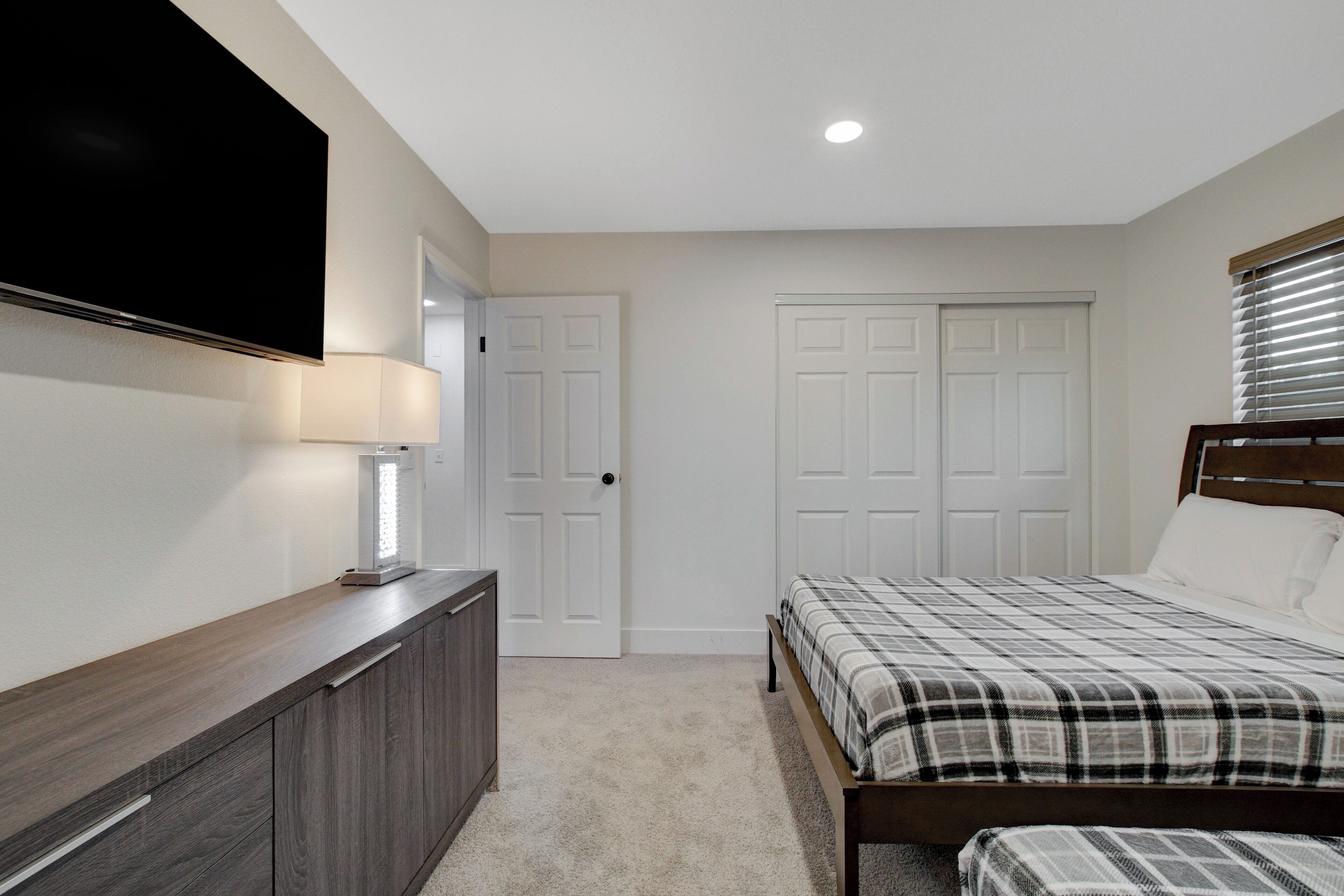 A bedroom with a bed, a TV mounted on the wall, a bedside table, and a door.