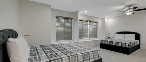 A bedroom with a bed, a window with blinds, a ceiling fan, and a nightstand.