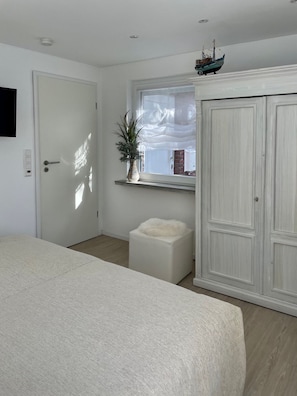 Une chambre à coucher avec un lit, une fenêtre ornée d’une plante, une armoire et une petite maquette de bateau posée sur le rebord de la fenêtre.