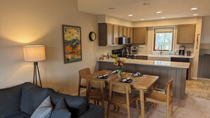 A modern kitchen with wooden cabinets, a central island, and a dining area with a table set for four. - Peaceful Fraser Condo Retreat, Close to Winter Park! (Fraser)